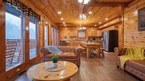 A log cabin interior with a dining area, kitchen, and seating.