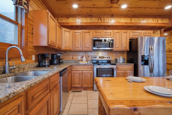 A kitchen with wooden cabinets, granite countertops, stainless steel appliances, and a wooden dining table.