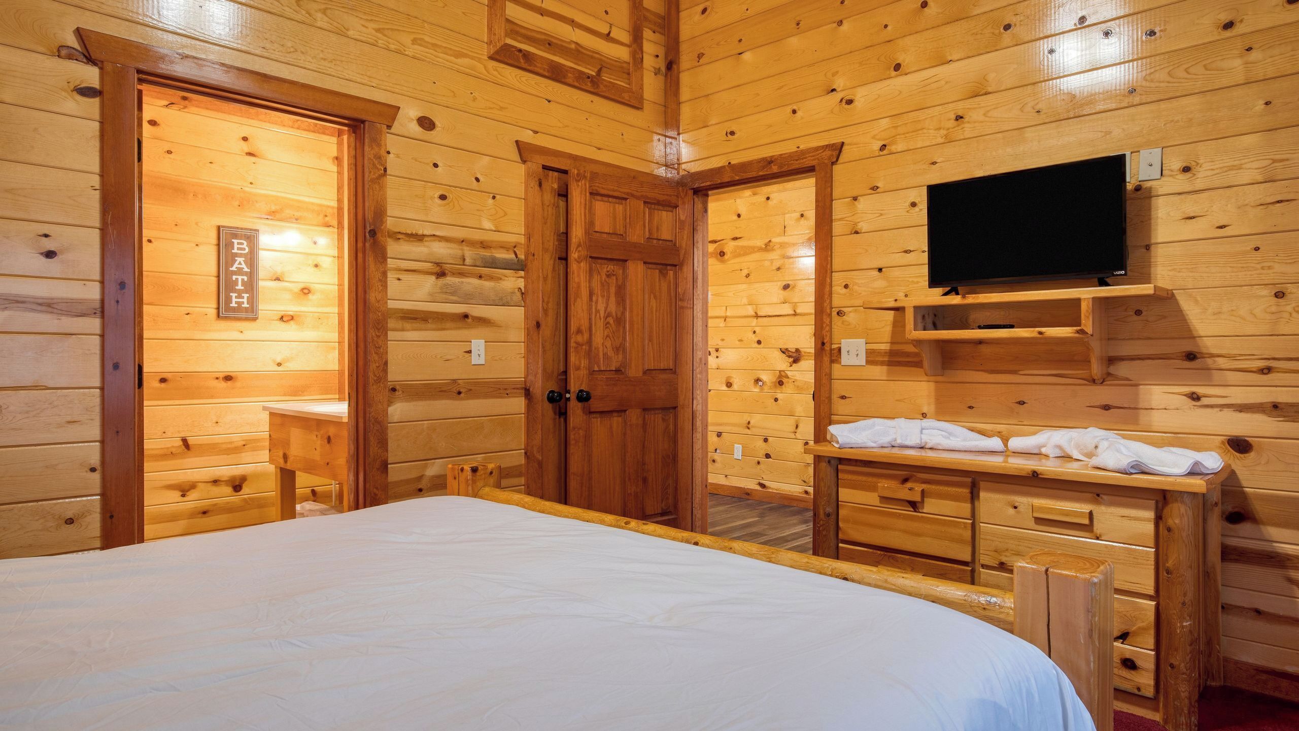 Habitación de cabaña de madera con una cama, un televisor y una mesita con toallas.
