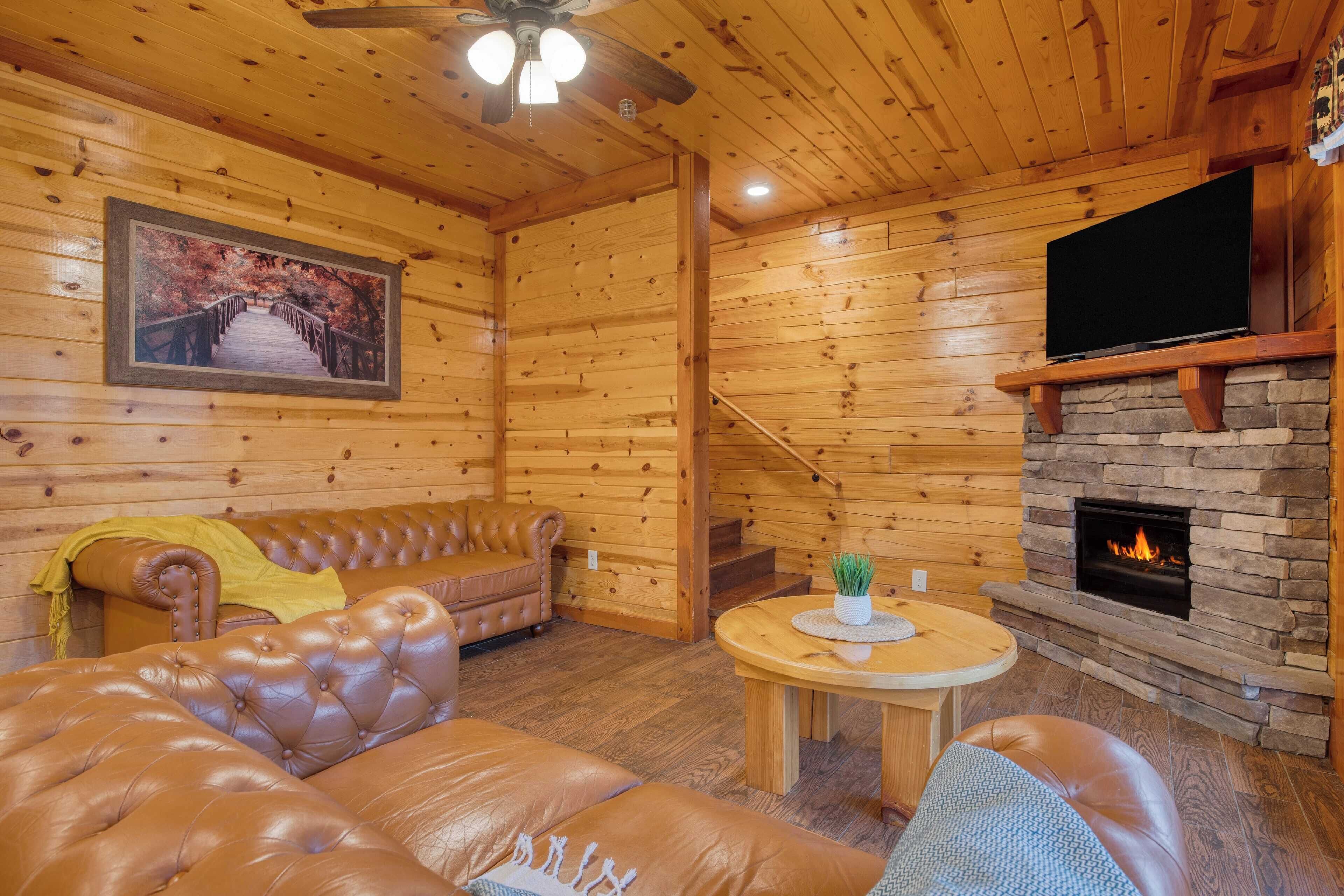 A cozy log cabin interior with a leather sofa, a fireplace, a television, and a painting of a bridge.
