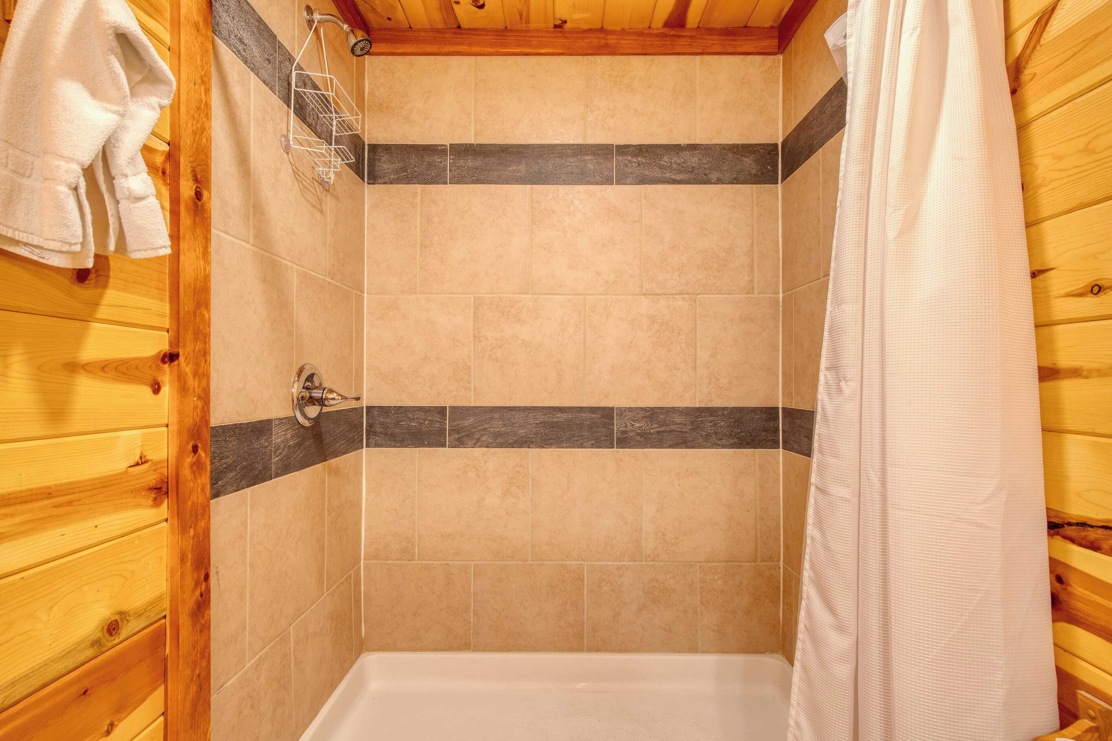A shower area with wooden walls, a tiled floor, and a white bathtub.