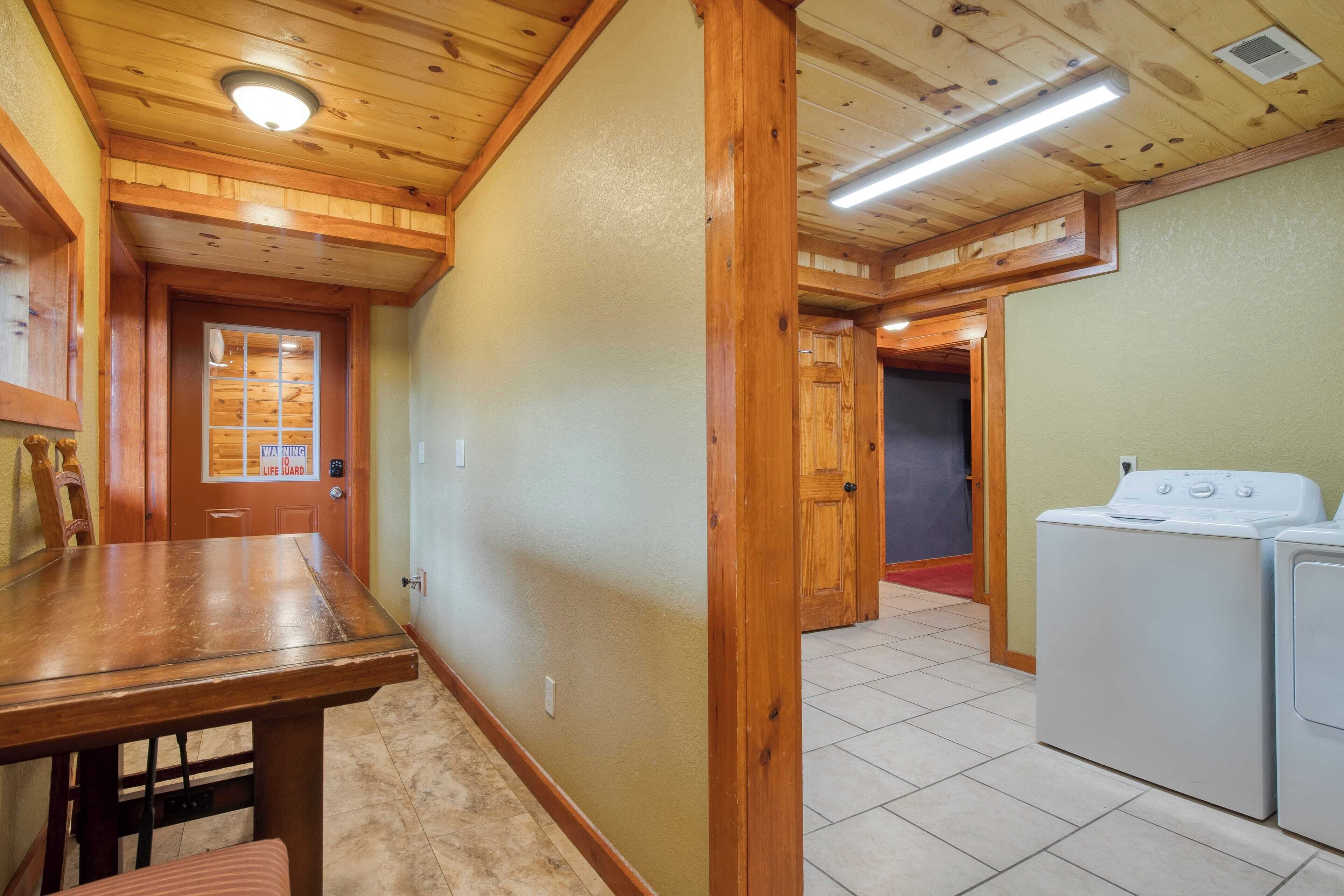 A laundry room with a washing machine and dryer, wooden ceiling beams, and a tiled floor.