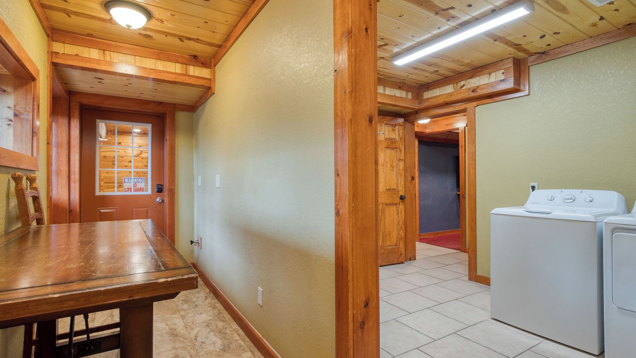 Interior de madera con una mesa, lavadora y una puerta con un letrero de advertencia.