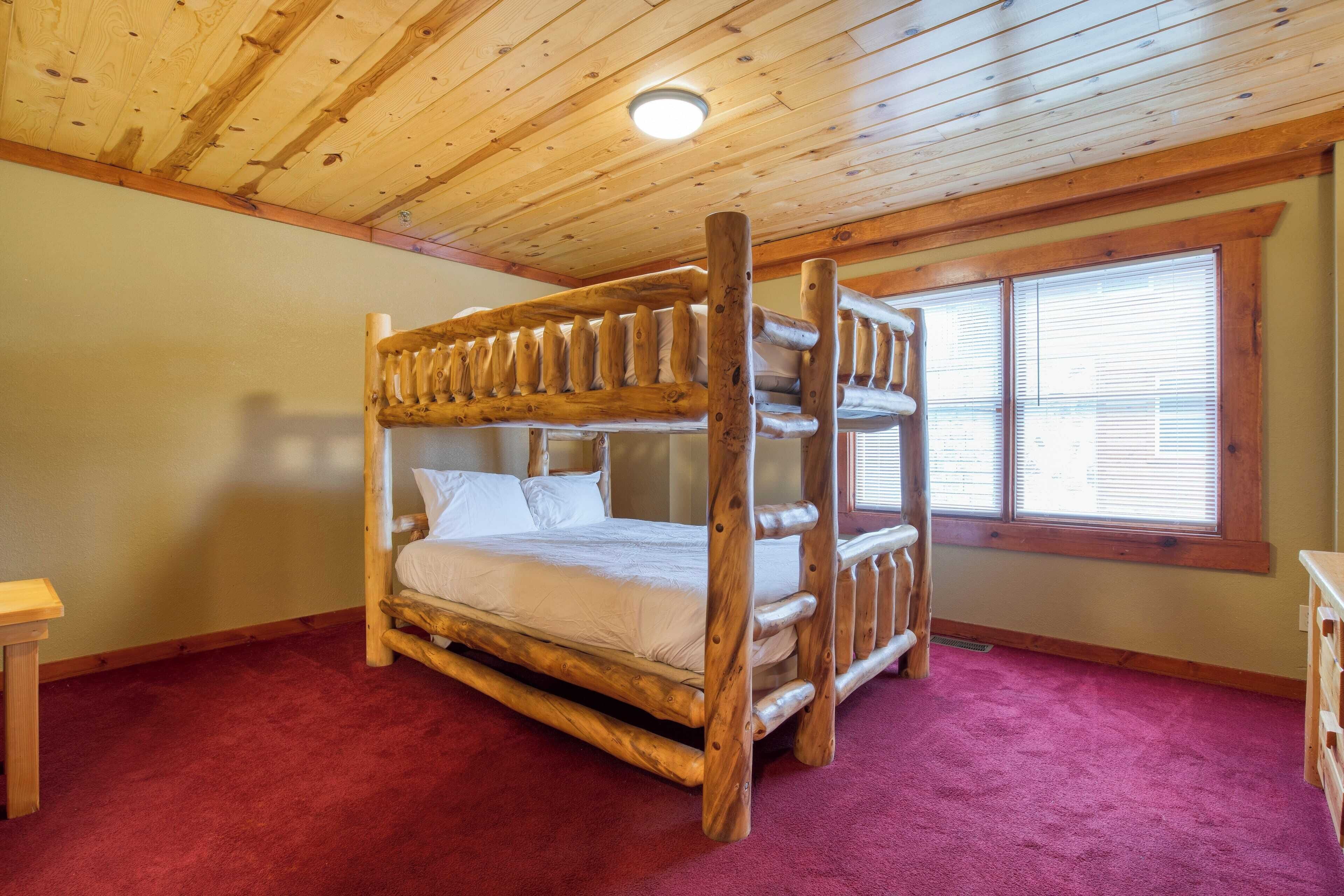 Una cama litera con estructura de madera en una habitación con alfombra roja, techo de madera y una ventana con persianas.