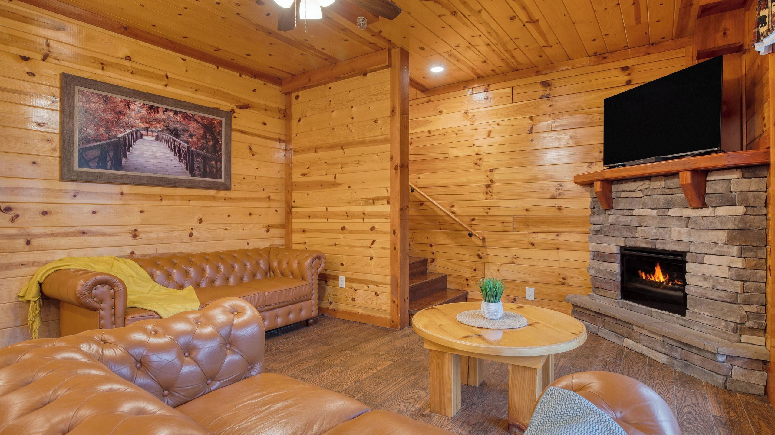 L’intérieur d’une cabane en rondins, avec un canapé en cuir, une cheminée, un téléviseur et un escalier.