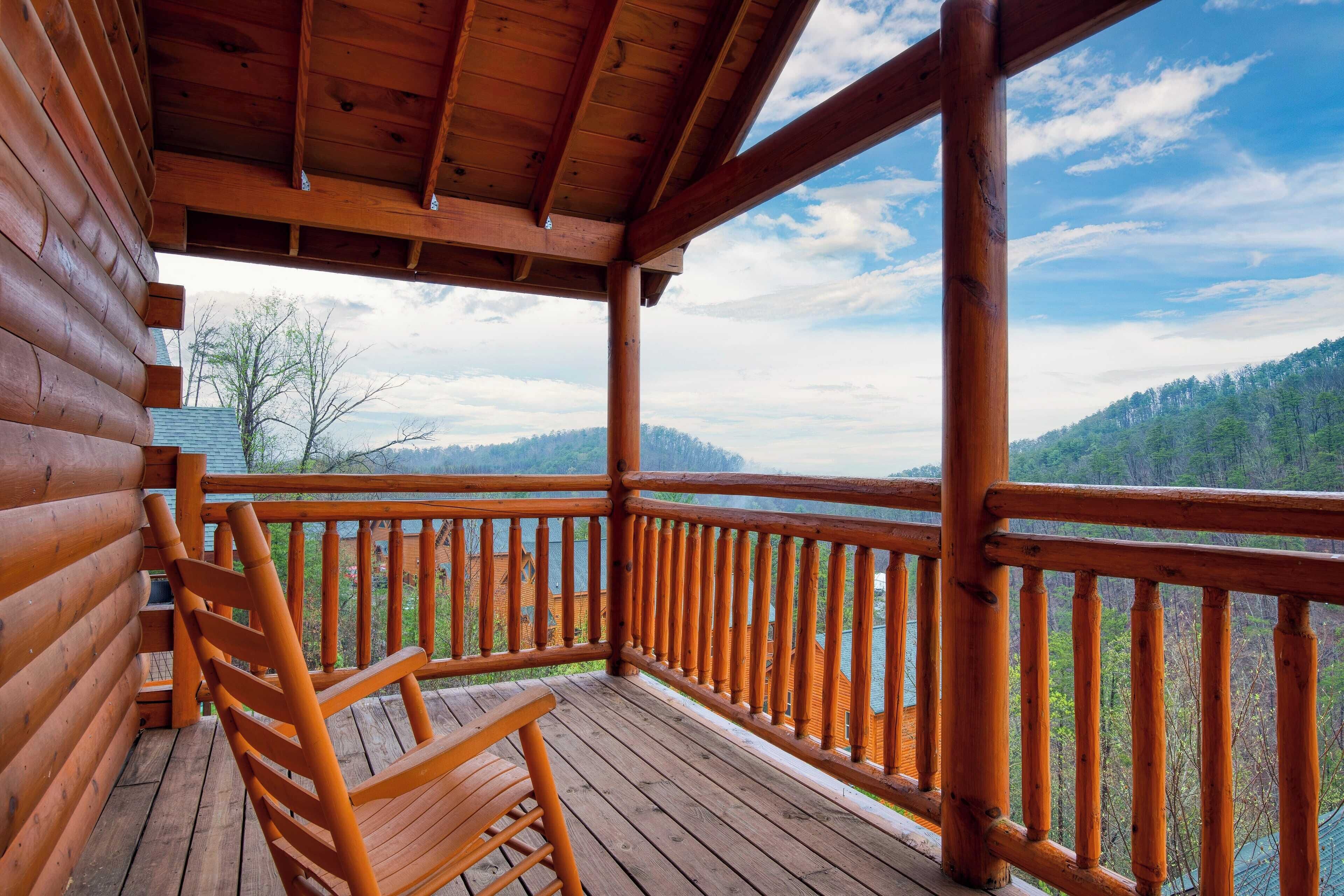 Una terraza de madera con una silla, barandilla y vistas a una cadena montañosa boscosa.