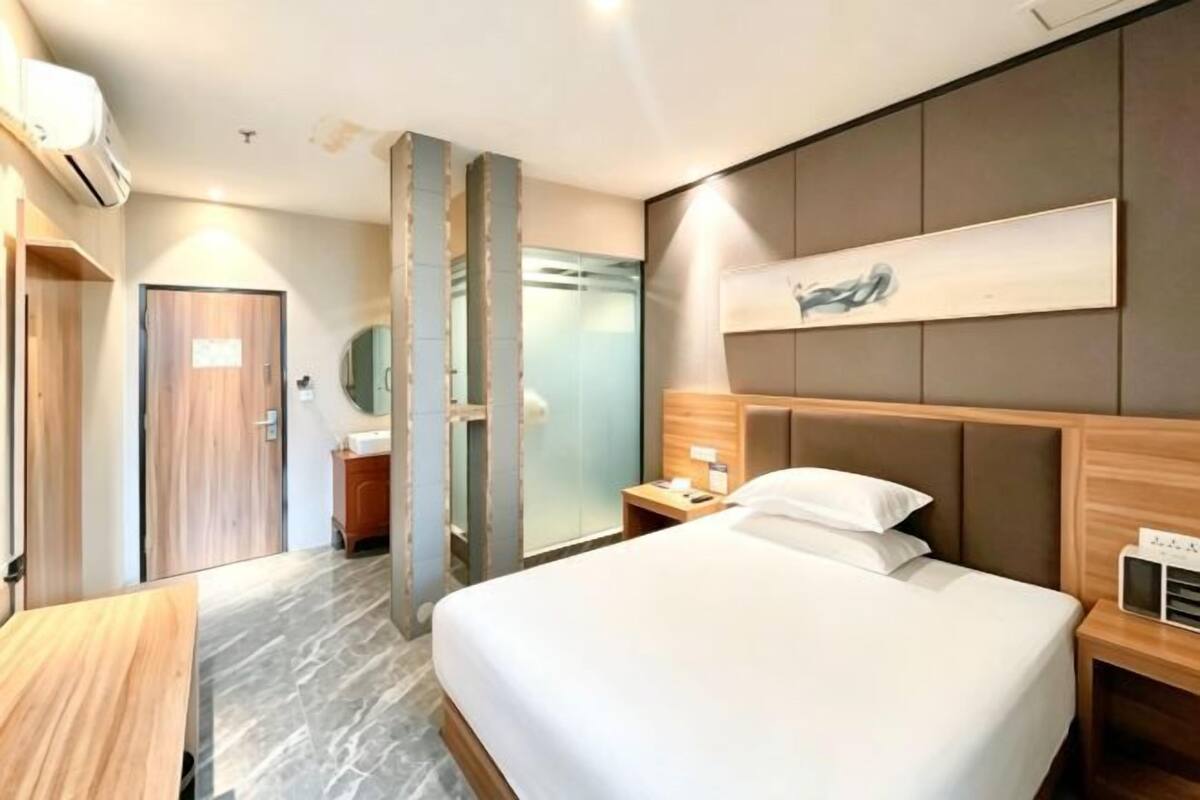 Habitación de hotel con cama, mesita de noche, obra de arte colgada en la pared y baño visible a través de un separador de vidrio.