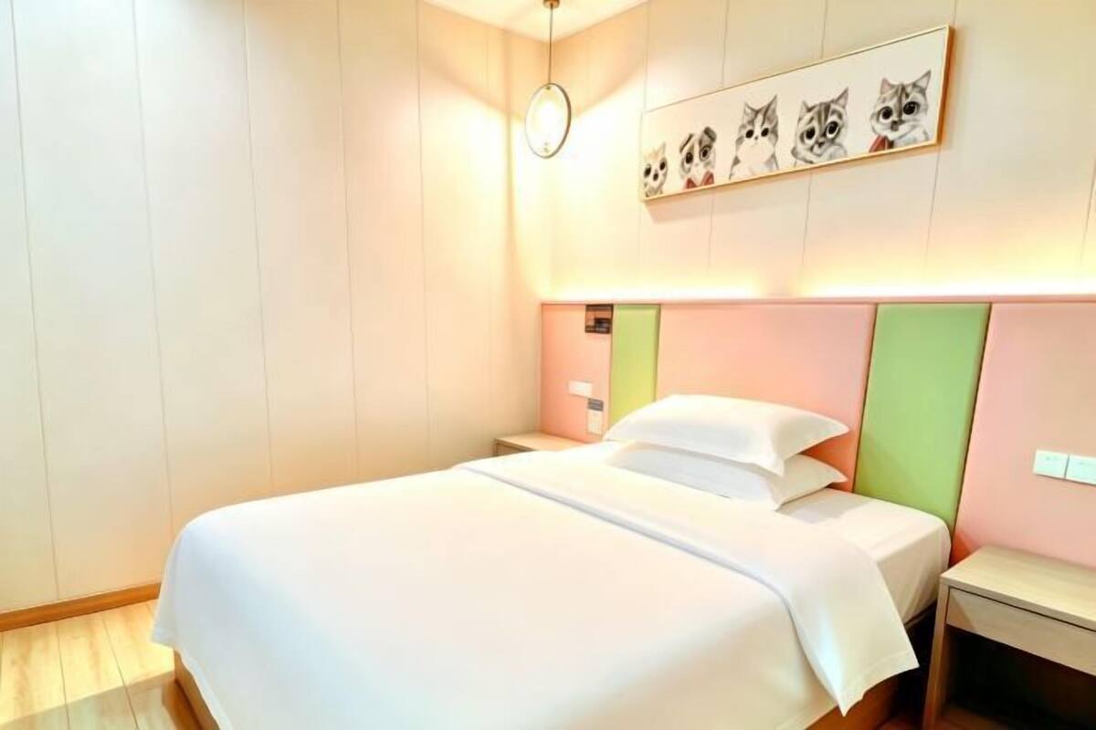 Una cama bien tendida en una habitación de hotel con un reloj de pared y varias fotografías enmarcadas sobre ella.