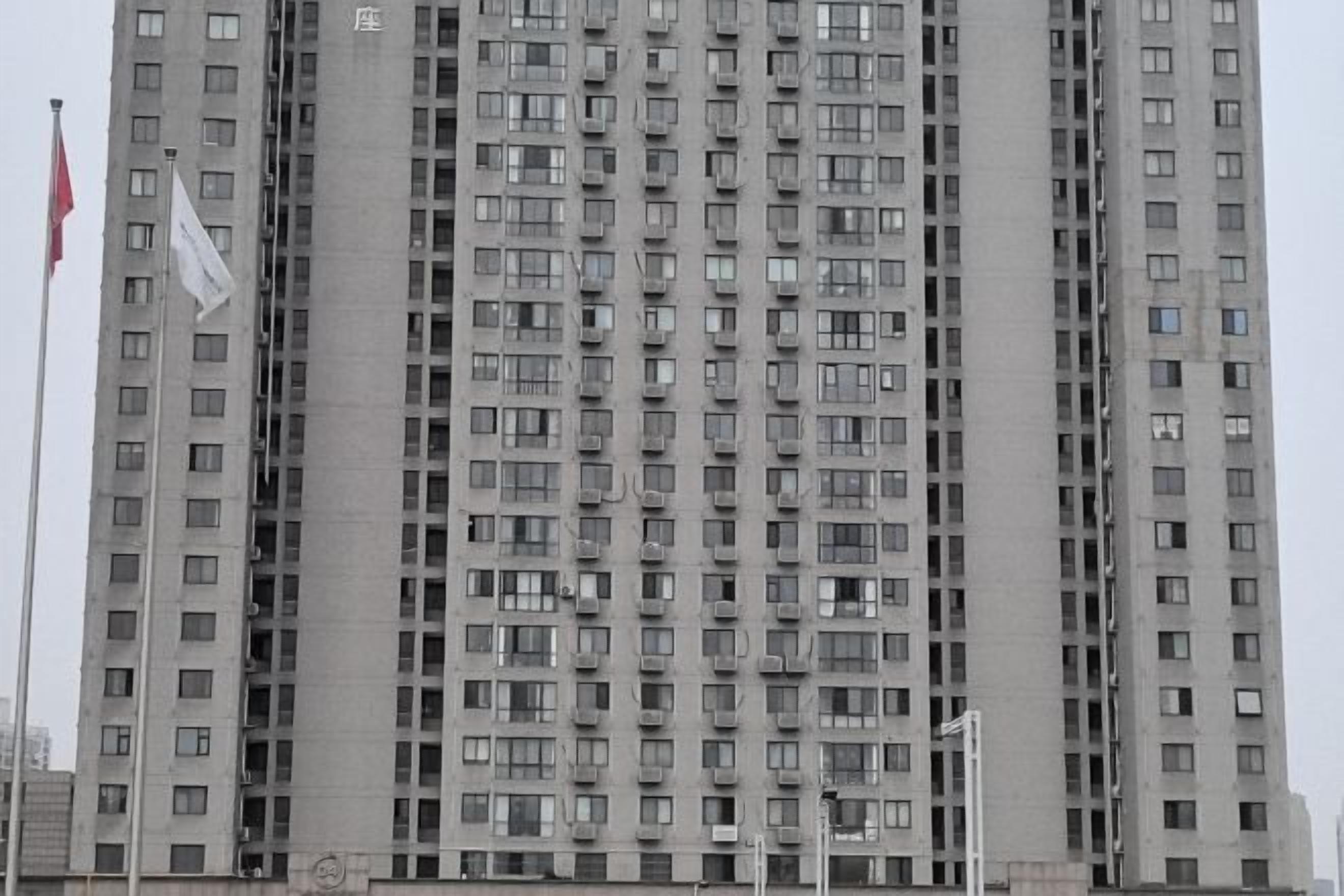 A high-rise building with multiple floors, numerous windows, and a flag on the left side.