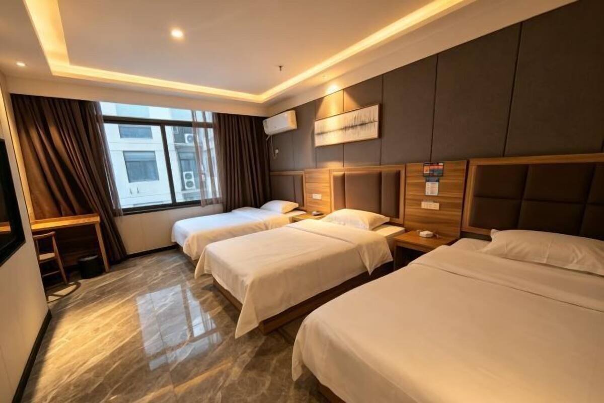 Habitación de hotel con tres camas, un escritorio y una ventana con cortinas.