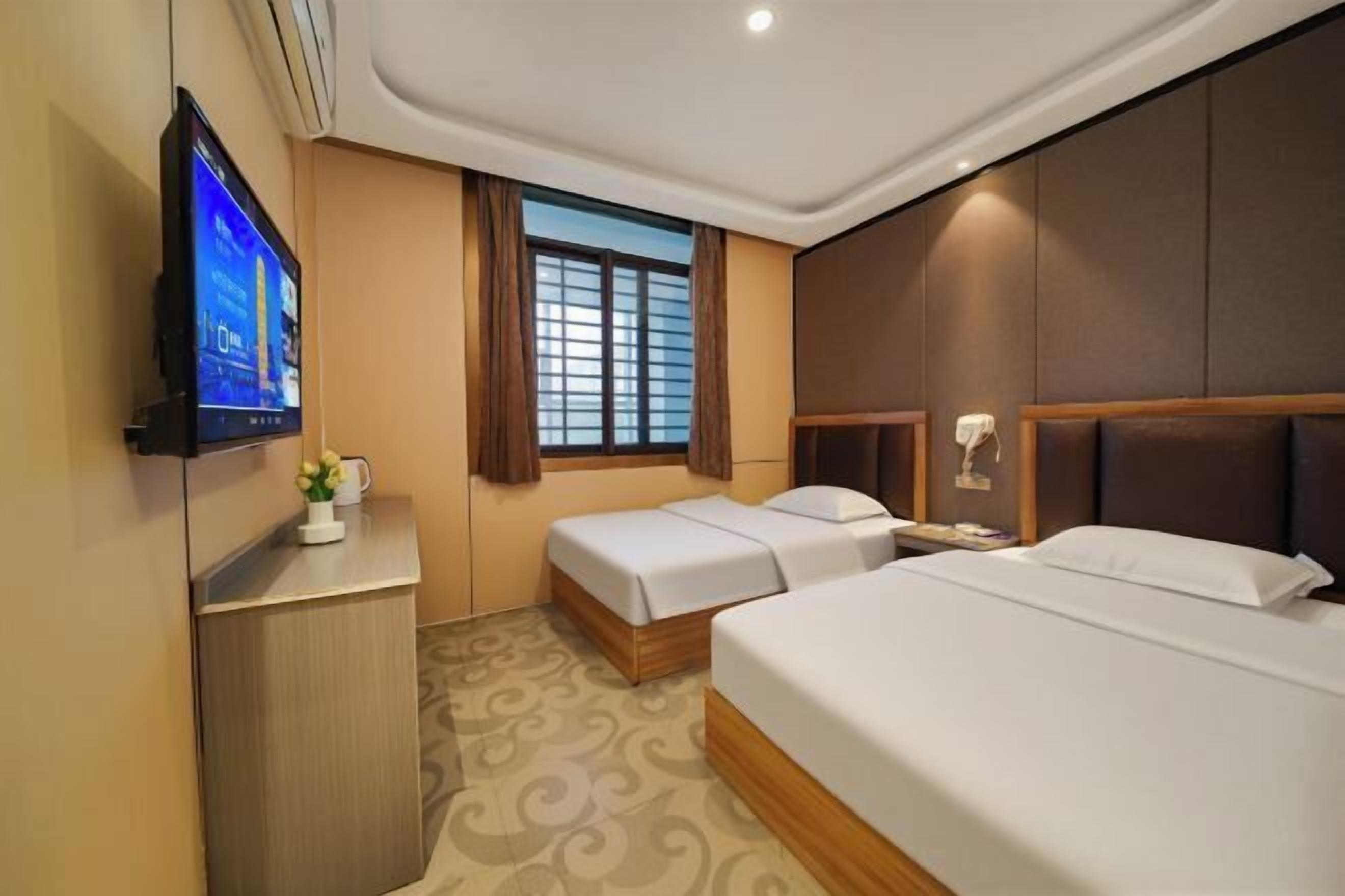 Ein Hotelzimmer mit zwei Betten, einem Fernseher, einem Schreibtisch mit einer Kaffeetasse und einem Fenster mit Vorhängen.