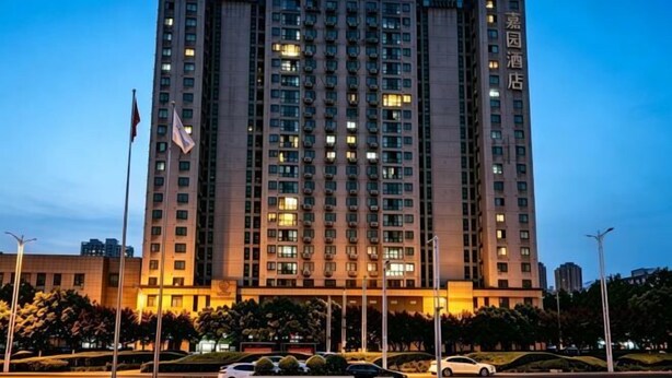 Un hotel de varios pisos con entrada central, bandera y ventanas iluminadas.