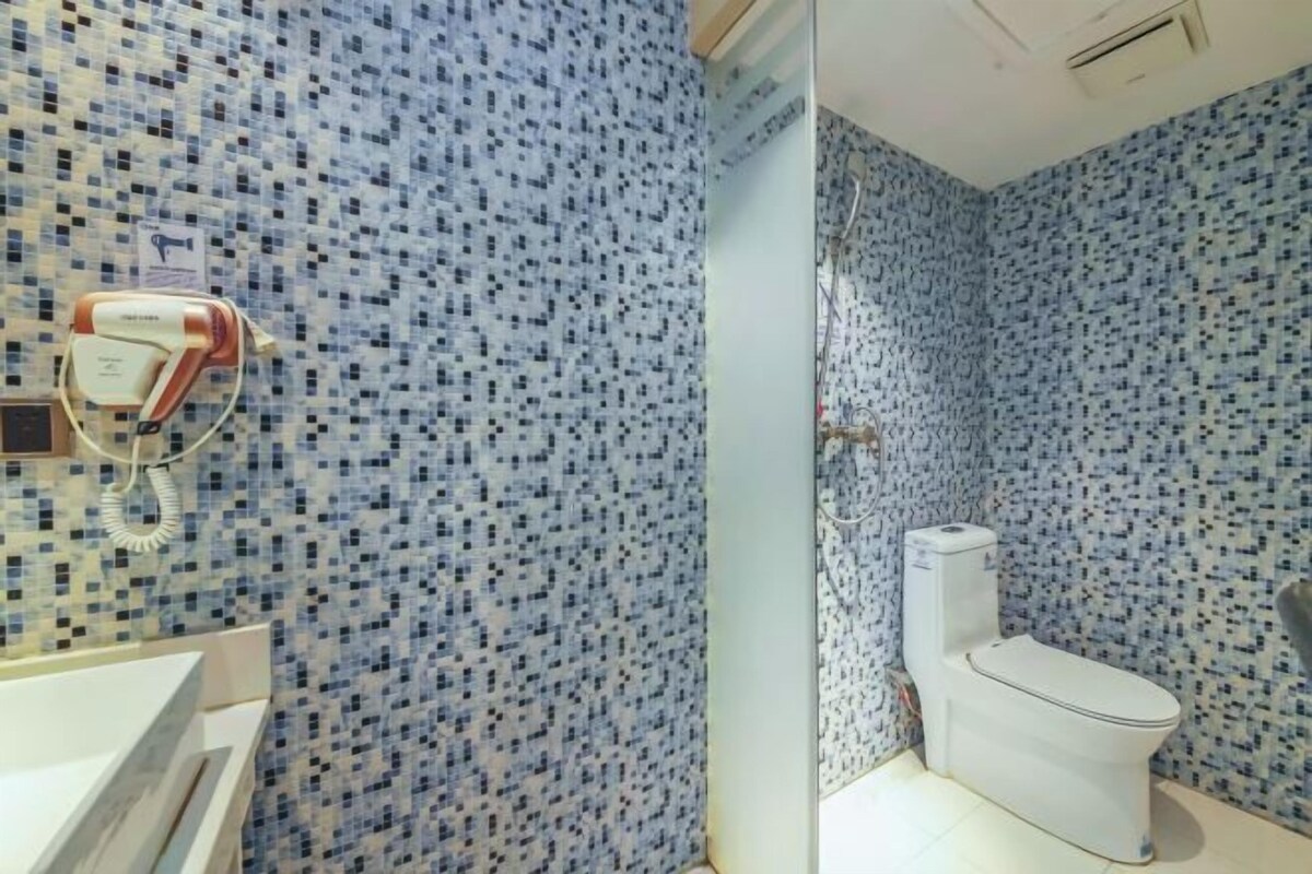 A bathroom with mosaic tile walls, a white toilet, and a hairdryer on the wall.