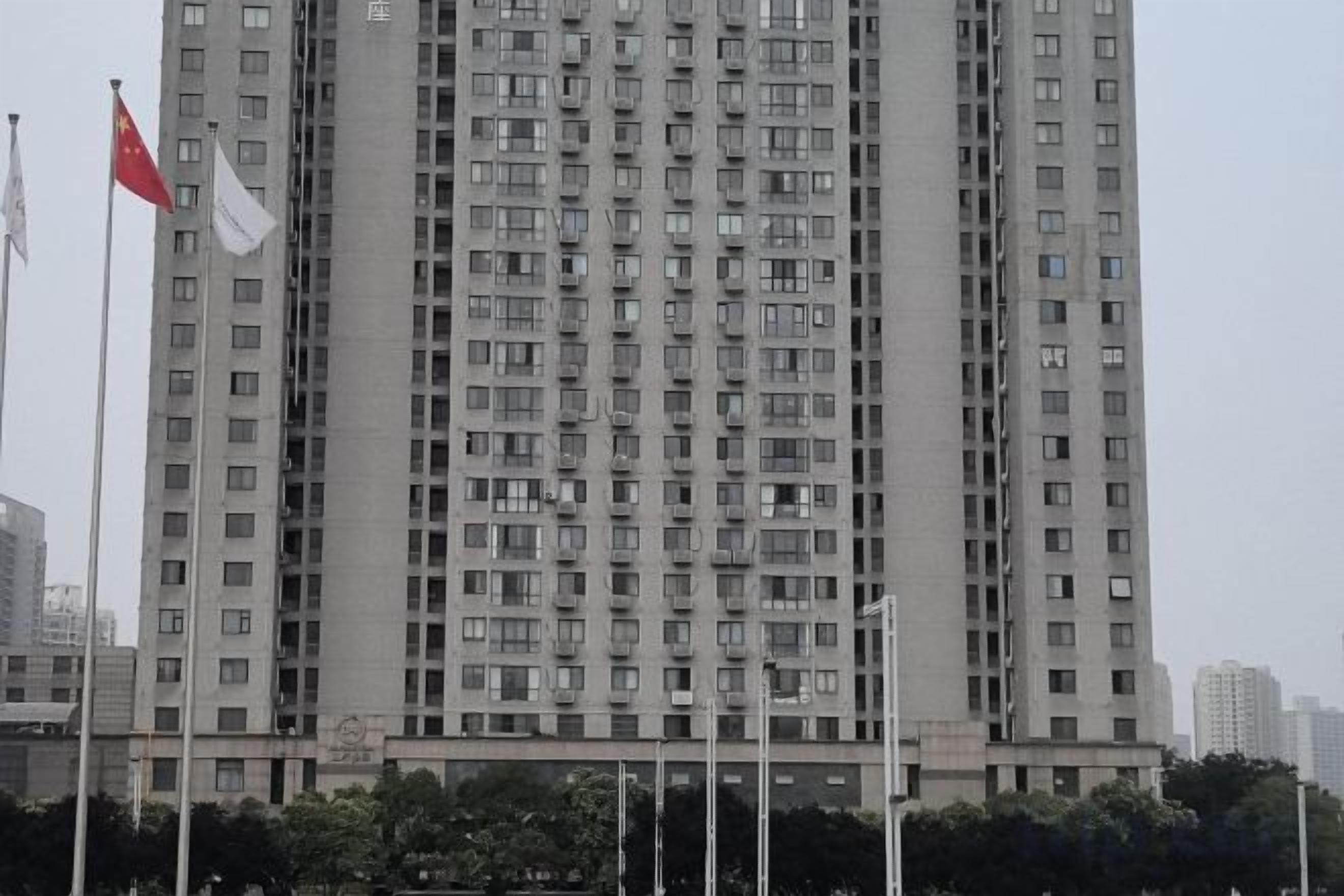 A tall building with a grid of windows, a flag on the left, and a clear sky.