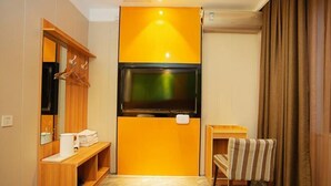 Habitación de hotel con una televisión montada en la pared, un banco de madera, una mesita con una toalla y un espejo.