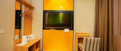 A hotel room with a television mounted on a wall, a wooden bench, a small table with a towel, and a mirror.