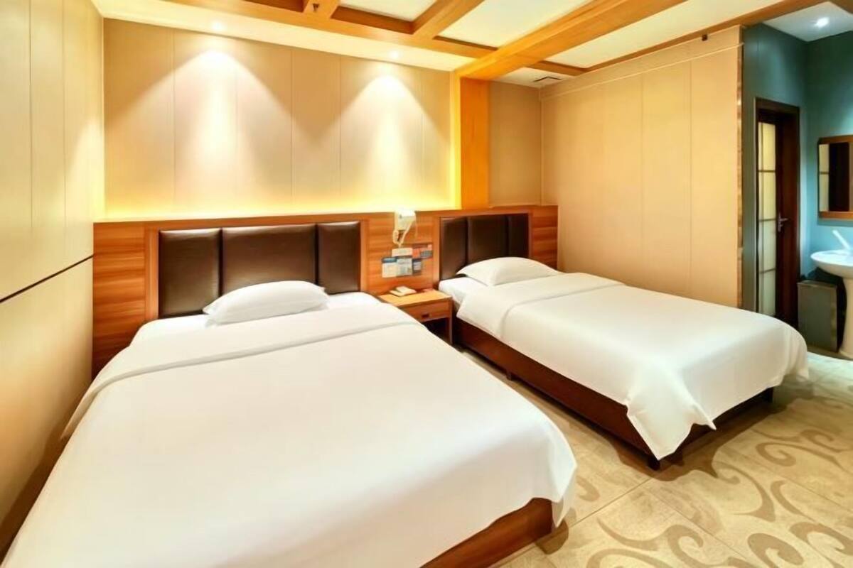 Una habitación de hotel con dos camas individuales, un cabecero de madera, una mesita de noche y otra mesilla.