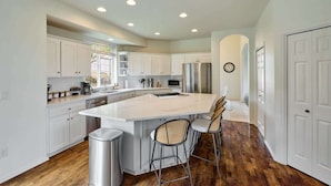 Una cocina moderna con armarios blancos, electrodomésticos de acero inoxidable, una isla grande con taburetes y suelo de madera.