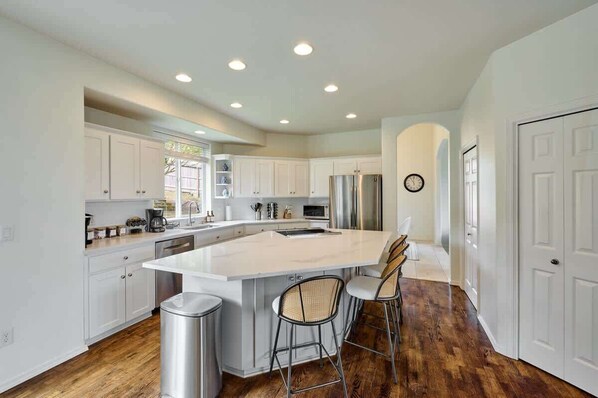 A modern kitchen with white cabinetry, stainless steel appliances, a large island with bar stools, and a wooden floor.