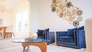 Una sala de estar con dos sofás azules, una mesa de centro de vidrio y una pared decorada con diseños circulares tejidos.