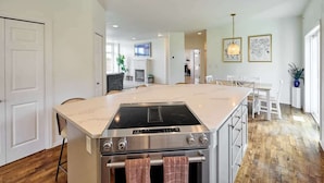 Una cocina moderna con una isla central, horno empotrado y comedor con mesa y sillas blancas.