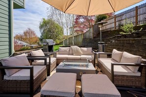 An outdoor patio with wicker furniture, a glass-top table, and a barbecue grill.