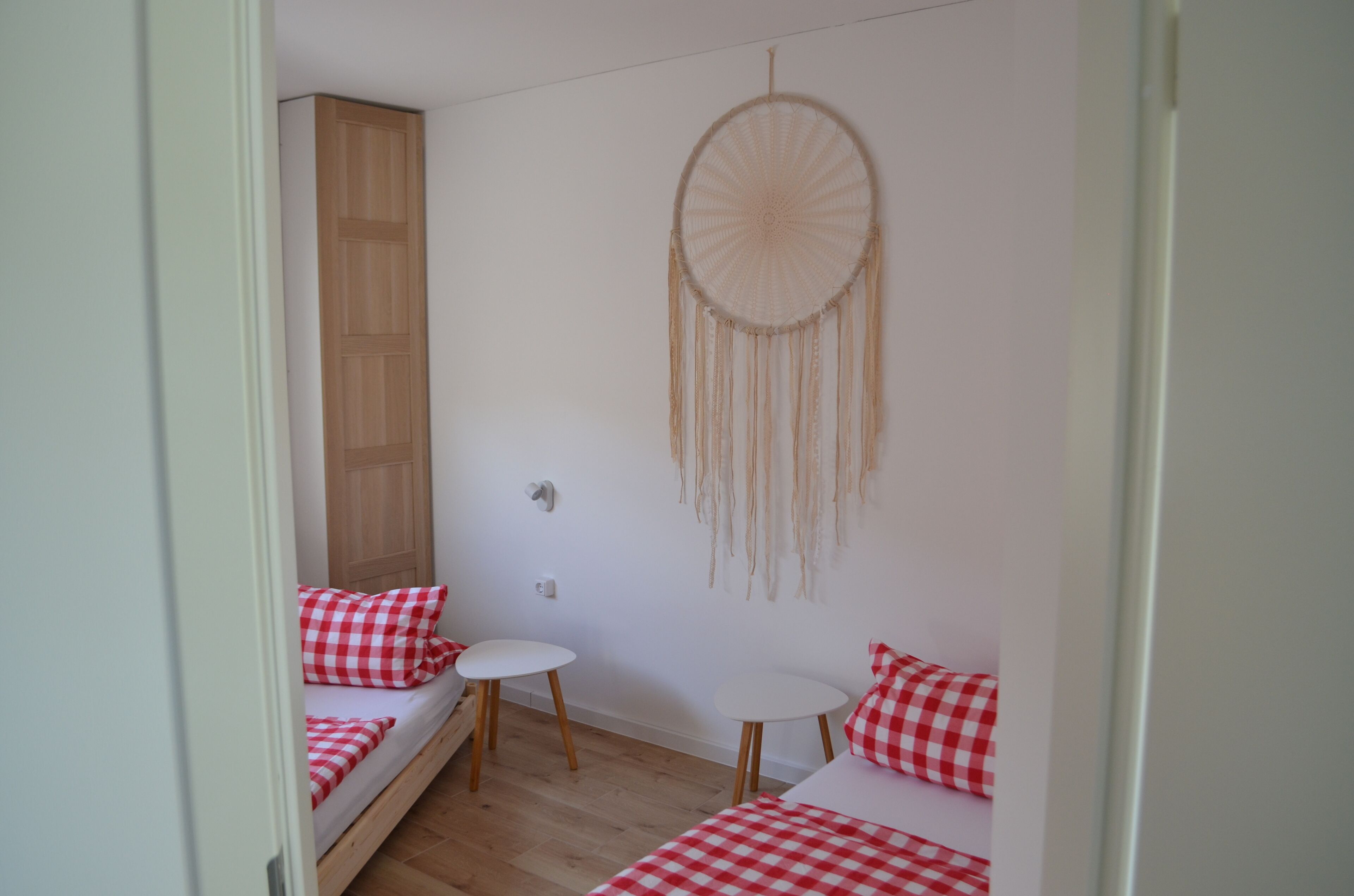 A small, cozy room with a bed, two small tables, and a dreamcatcher on the wall.