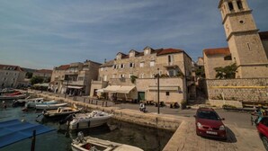 Un pueblo costero con edificios de piedra, una torre destacada con reloj y barcos amarrados a lo largo del muelle.