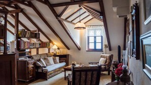 Un acogedor dormitorio en ático con vigas de madera a la vista, un sofá, una silla, una mesa y una estantería llena de libros.
