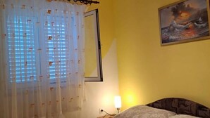 A bedroom with a bed, a nightstand, a lamp, a painting, and a window with curtains. - Apartments Dana - Two Bedroom Apartment 1 (Srima)
