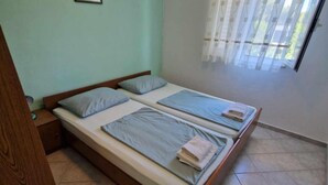 A room with a double bed, two pillows, a wooden nightstand, and a window with curtains.