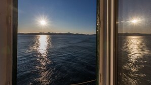 A view of the sea with the sun reflecting off the water, visible through a window with a metal frame. - Charming Apartment in Zadar with City Views - Three Bedroom Apartment (Zadar)