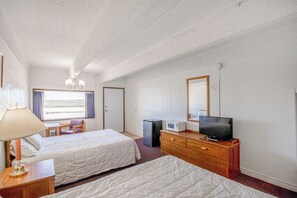 A hotel room with two beds, a desk, a chair, a TV, a dresser, a lamp, and a window with curtains.