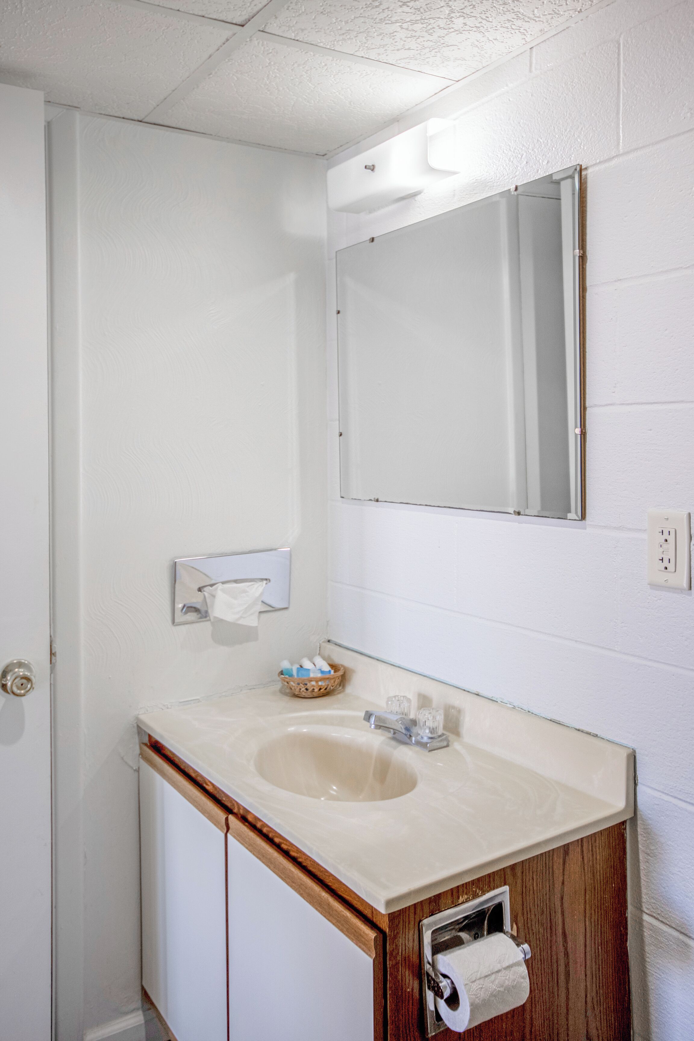 Un baño con lavamanos blanco, mueble de madera y espejo sobre el lavamanos.
