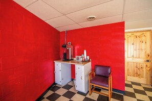 A room with red walls, a checkered floor, a desk with a chair, and a wooden door.