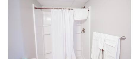 A shower with a white curtain, a white towel rack, and a green toilet tissue dispenser.