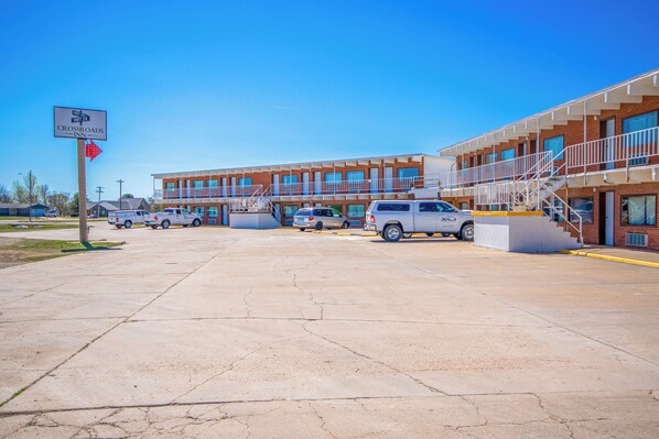 A motel with multiple floors, a parking lot with several vehicles, and a clear blue sky.