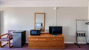 Une pièce de taille modeste, comprenant une commode en bois, un petit réfrigérateur, une télévision, un miroir et un porte-vêtements.