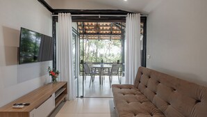 A modern living room with a sofa, TV, and a dining area with chairs and a table. - SUNSET PORTO BELO locaçoes (Porto Belo)