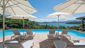 A poolside area with white lounge chairs and umbrellas, overlooking a scenic body of water and city skyline. - SUNSET PORTO BELO locaçoes (Porto Belo)