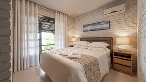 A bedroom with a bed, bedside tables, a window with curtains, a wall-mounted air conditioner, and a painting. - SUNSET PORTO BELO locaçoes (Porto Belo)