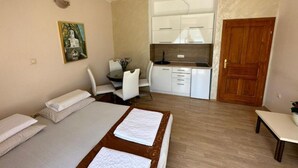 A compact room with a bed, a small dining table with chairs, a kitchenette, and a wooden door.