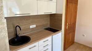 A compact kitchen with white cabinets, a black sink, and a wooden countertop.