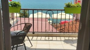 A balcony with a view of the sea, a chair, and potted plants.