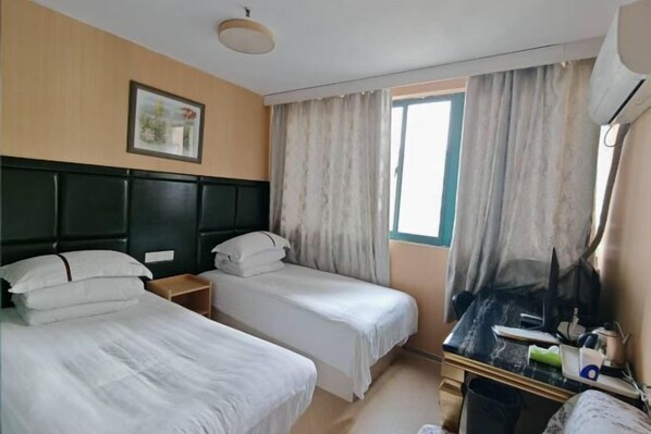A hotel room with two single beds, a desk with a chair, a window with curtains, a picture on the wall, and an air conditioning unit. - Shanghai Maoyi Hotel (Shanghai)