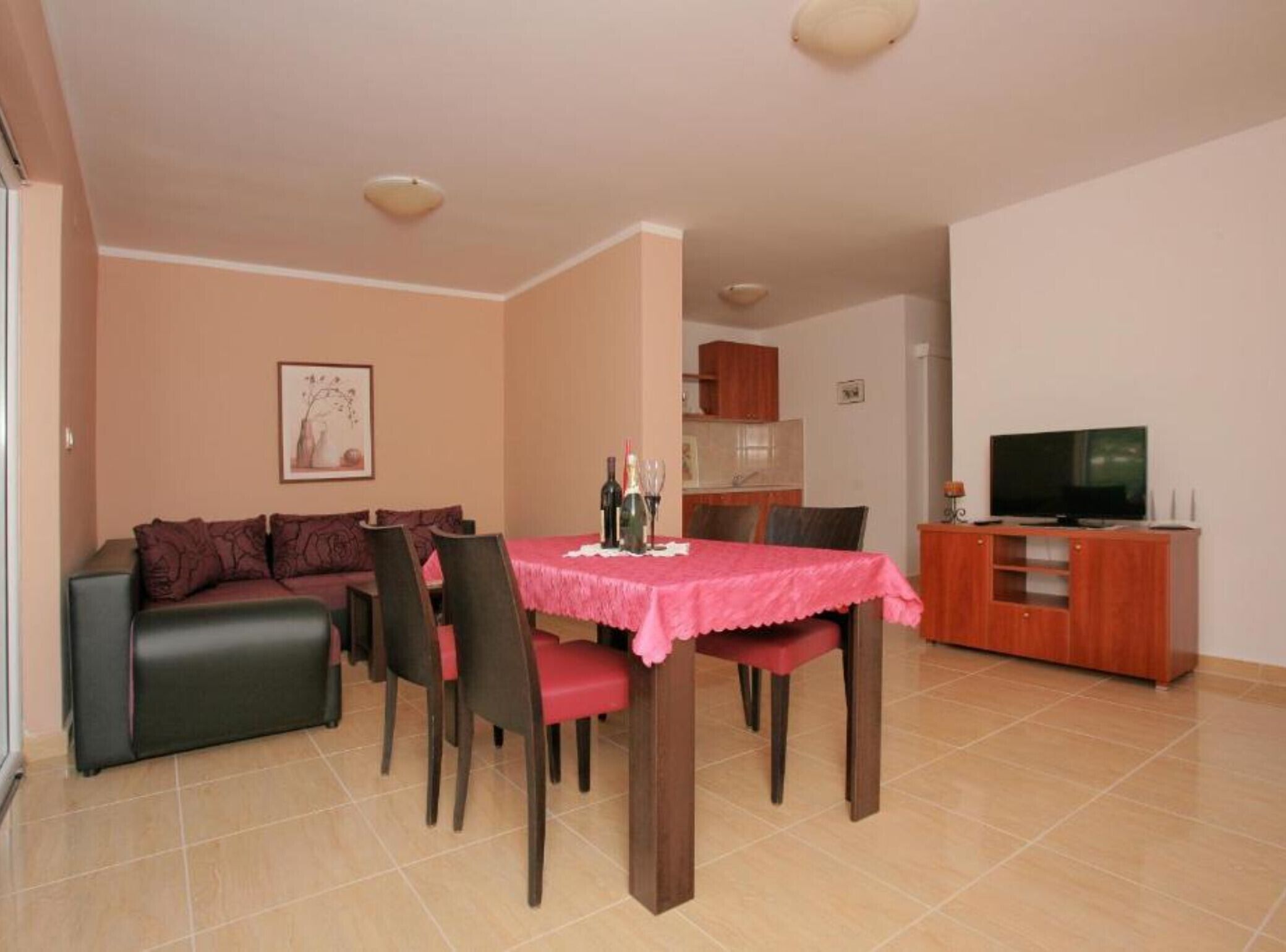 A dining area with a table set for four, a sofa, and a television on a wooden cabinet.