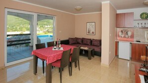 Un coin repas avec une table dressée pour deux personnes, un canapé et un espace cuisine équipé de placards et d’un four à micro-ondes.