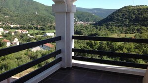 A balcony with a view of a green valley and distant buildings.