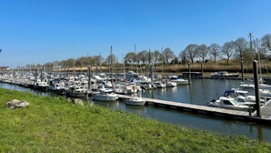 A marina with numerous boats docked along the water's edge, surrounded by grassy banks and trees.