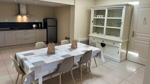 A modern kitchen with a dining area, featuring a table with chairs, a cabinet with glass doors, and a skylight above.